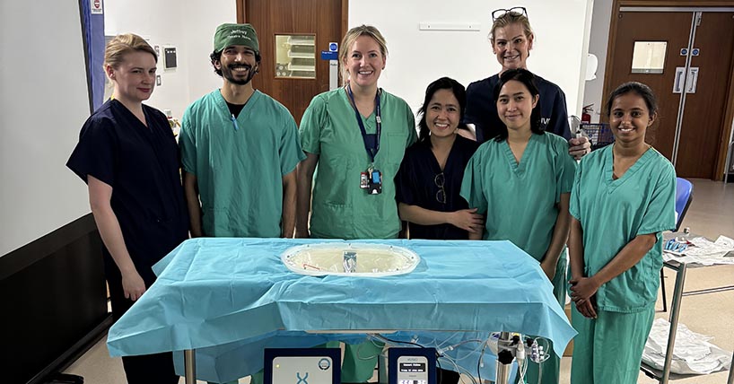 surgeon and team in green scrubs round a table with a blue cloth surgeon and team in green scrubs round a table with a blue cloth